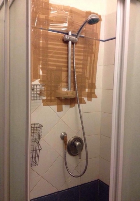 nietypowo przytwierdzony do ściany prysznic za pomocą taśmy klejącej