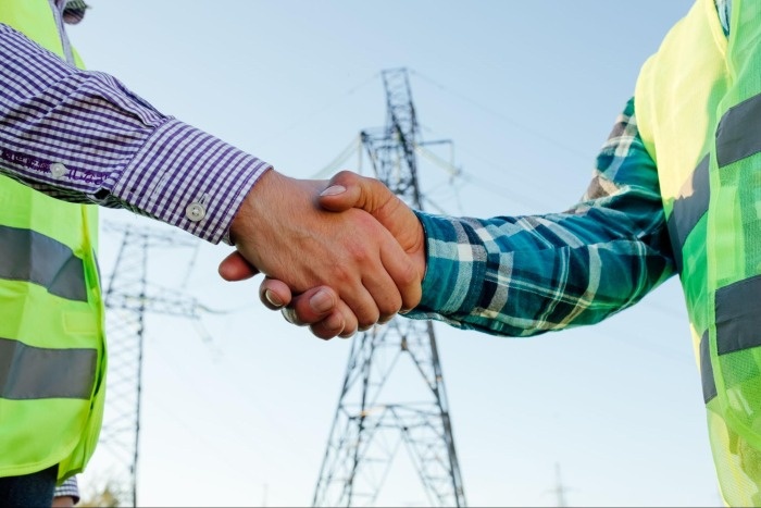 mężczyźni podający sobie rękę na tle słupa energetycznego
